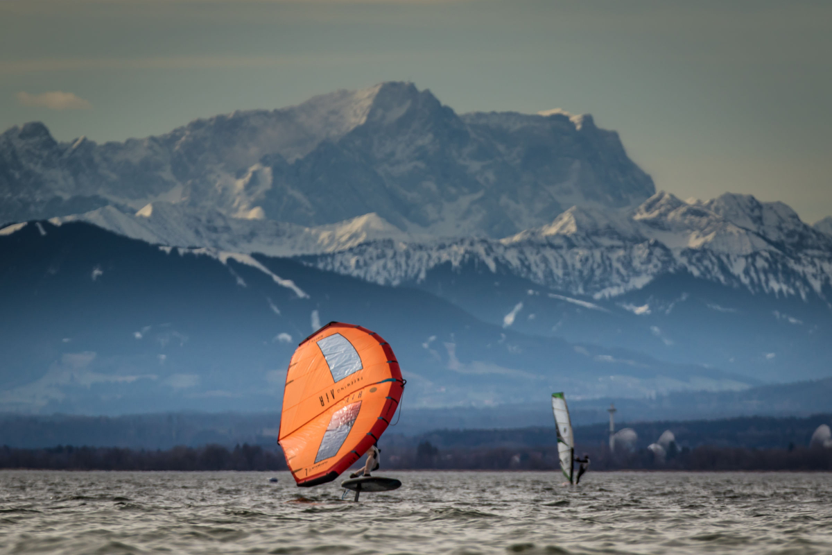 Carsten Kurmis lässt sein Foilboard vor verschneiter Alpenkulisse fliegen